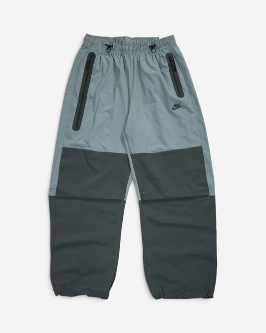 Сіро-чорні вільні штани Nike Tech Woven Oversized з еластичним поясом на затяжках, вертикальними блискавками з боків та чорним логотипом на стегні.