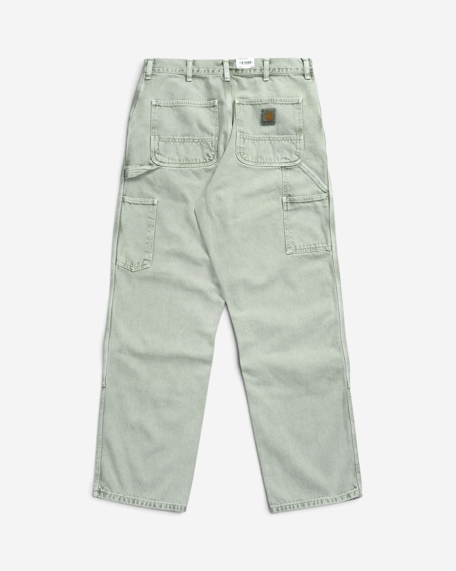 Світло-зелені робочі штани Carhartt WIP Double Knee Pant, вигляд ззаду, з утилітарними робочими кишенями, потертим ефектом та квадратним логотипом бренду.