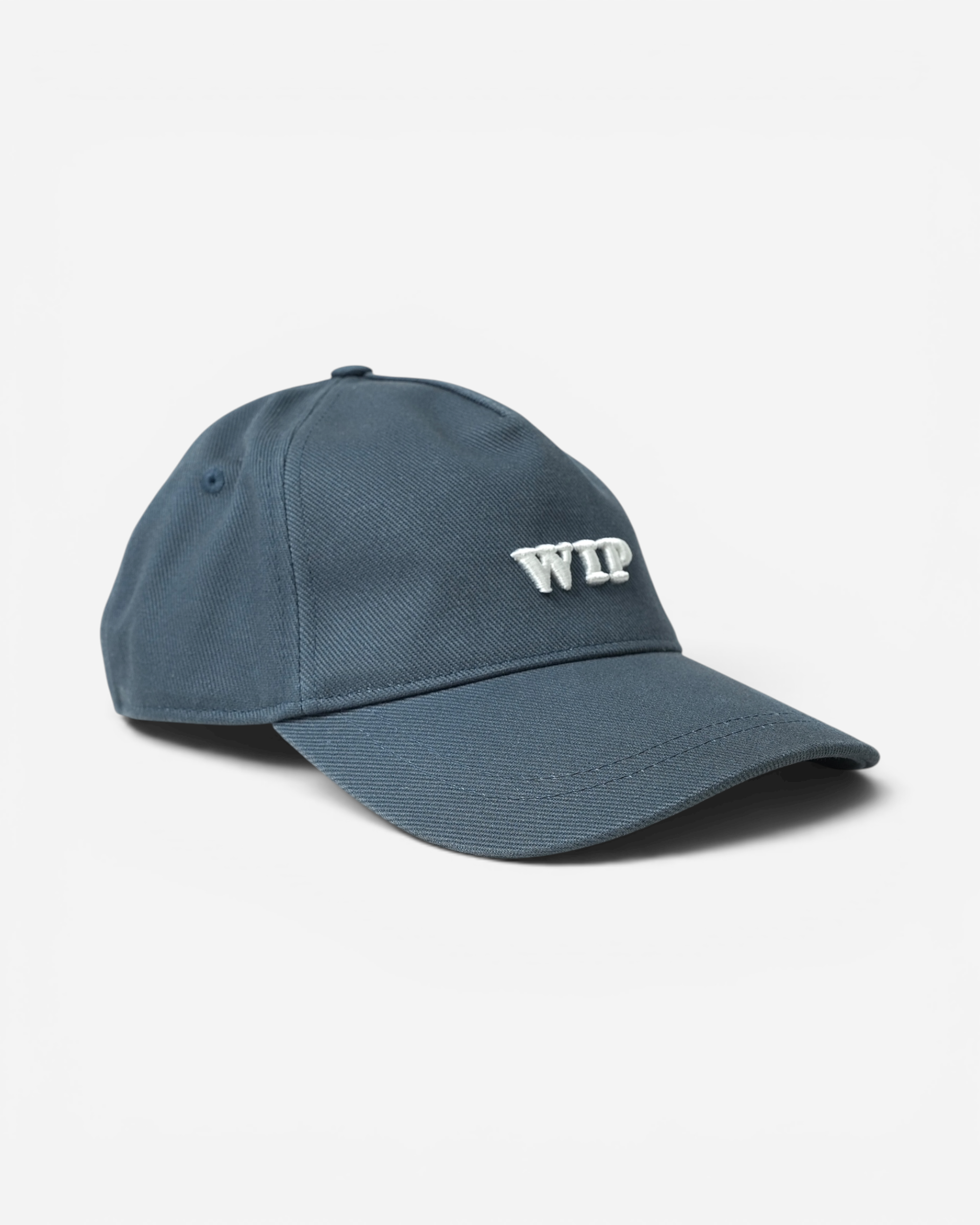 Сіро-синя бавовняна кепка Carhartt WIP із твердим вигнутим козирком та великою об'ємною білою вишивкою літер WIP на фронтальній панелі.