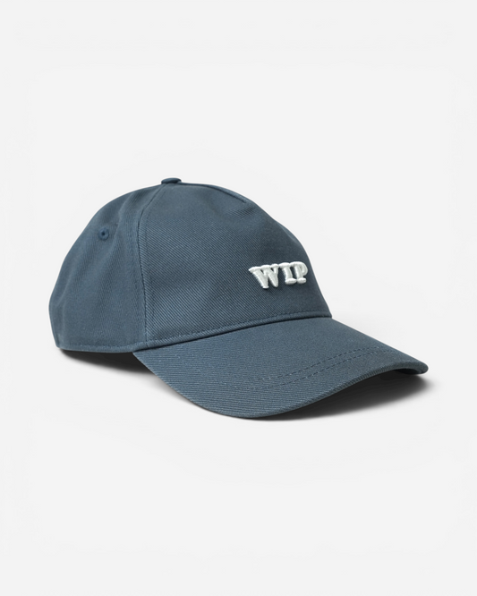 Сіро-синя бавовняна кепка Carhartt WIP із твердим вигнутим козирком та великою об'ємною білою вишивкою літер WIP на фронтальній панелі.