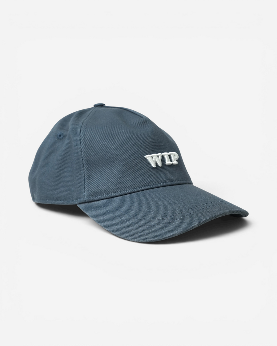 Сіро-синя бавовняна кепка Carhartt WIP із твердим вигнутим козирком та великою об'ємною білою вишивкою літер WIP на фронтальній панелі.