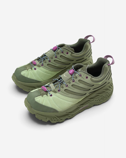 Оливково-зелені кросівки Hoka Stinson Evo OG із товстою підошвою, яскраво-фіолетовими петлями, фіолетовим фіксатором та шнурівкою.