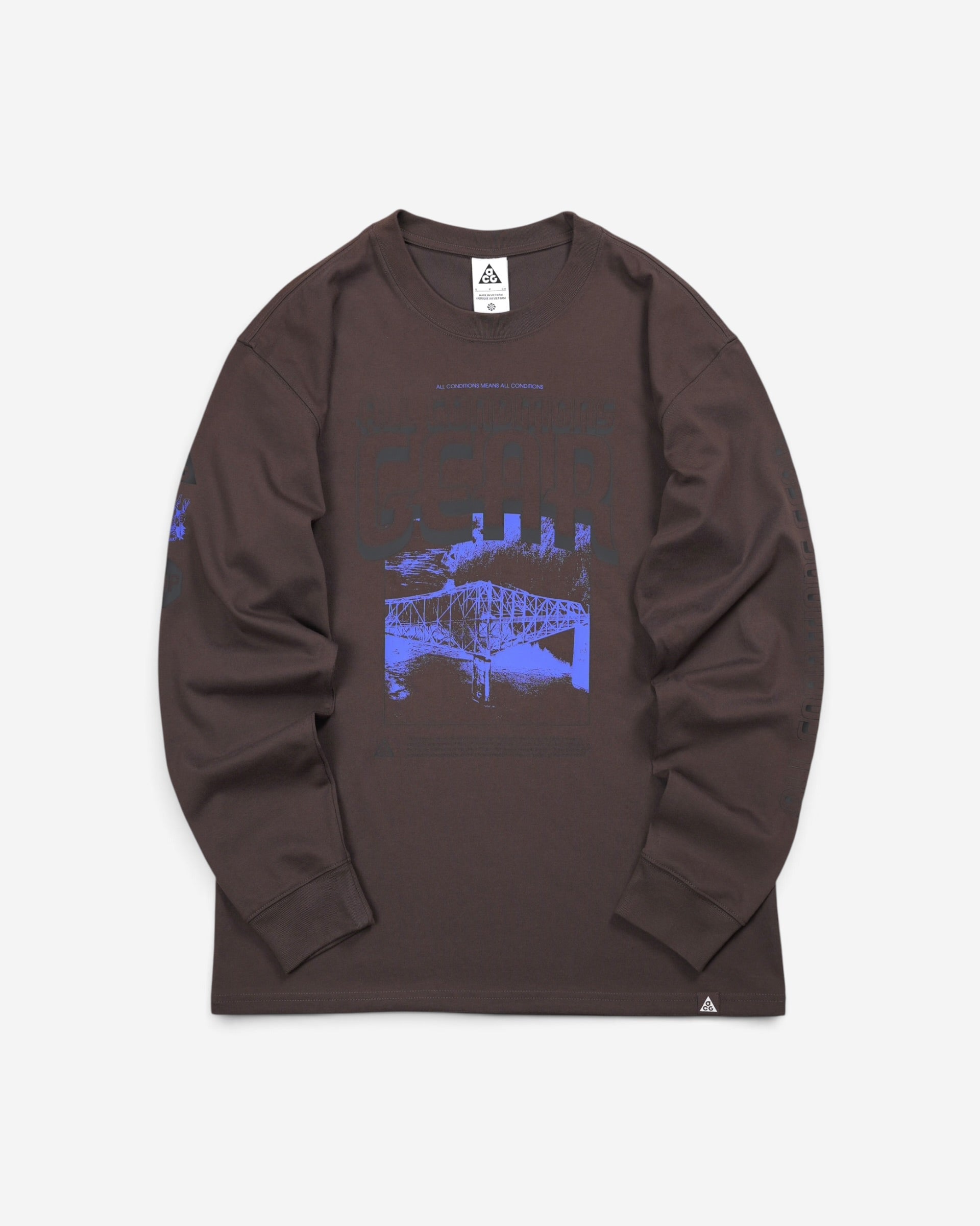  Темно-коричневий лонгслів Nike ACG Bridge of Gods Long-Sleeve T-Shirt з яскравим синім принтом моста на грудях та малюнками на рукавах.
