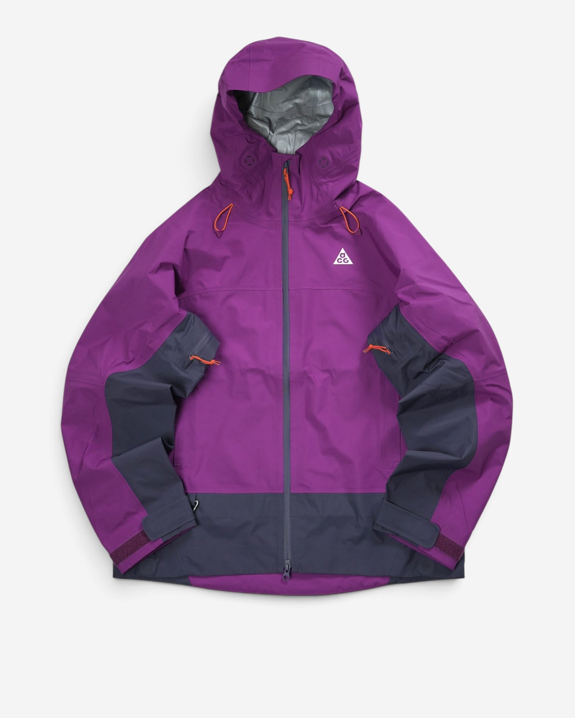 Чоловіча штормова куртка Nike ACG фіолетового кольору з темно-сірими панелями на подолі та рукавах, високим коміром і білим трикутним логотипом на грудях.
