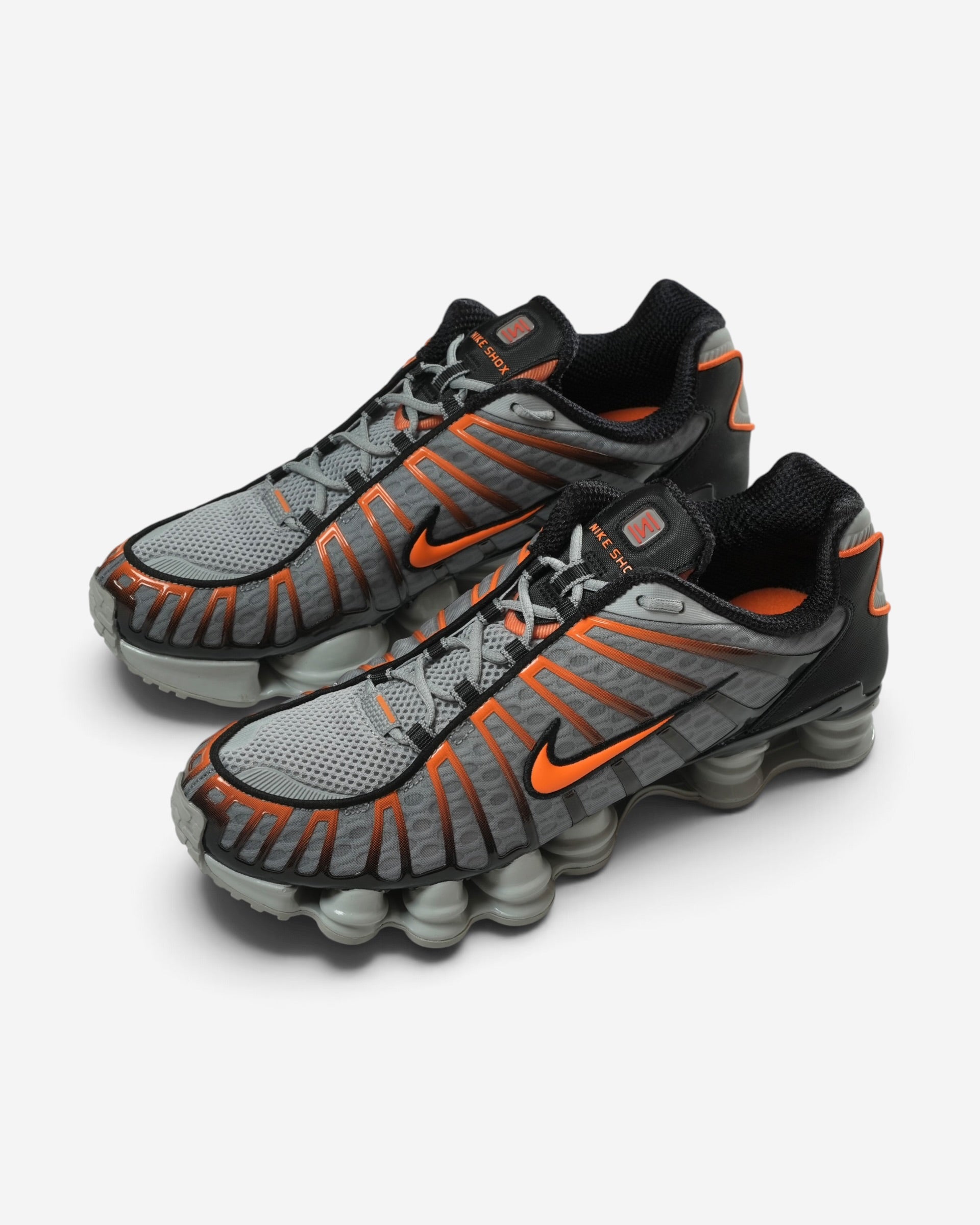 Сіро-чорні чоловічі кросівки Nike Shox TL із яскраво-помаранчевими лініями каркаса, помаранчевим логотипом та впізнаваною пружинною подошвою.