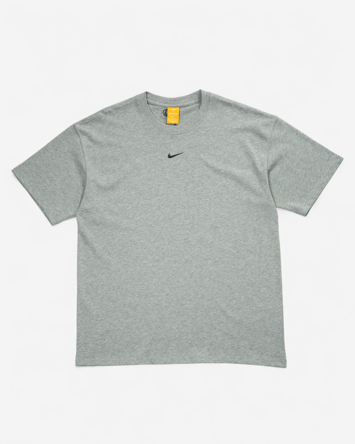 Меланжева сіра футболка вільного оверсайз крою Nike x NOCTA з маленьким чорним свушем по центру грудей та помаранчевою біркою на горловині.