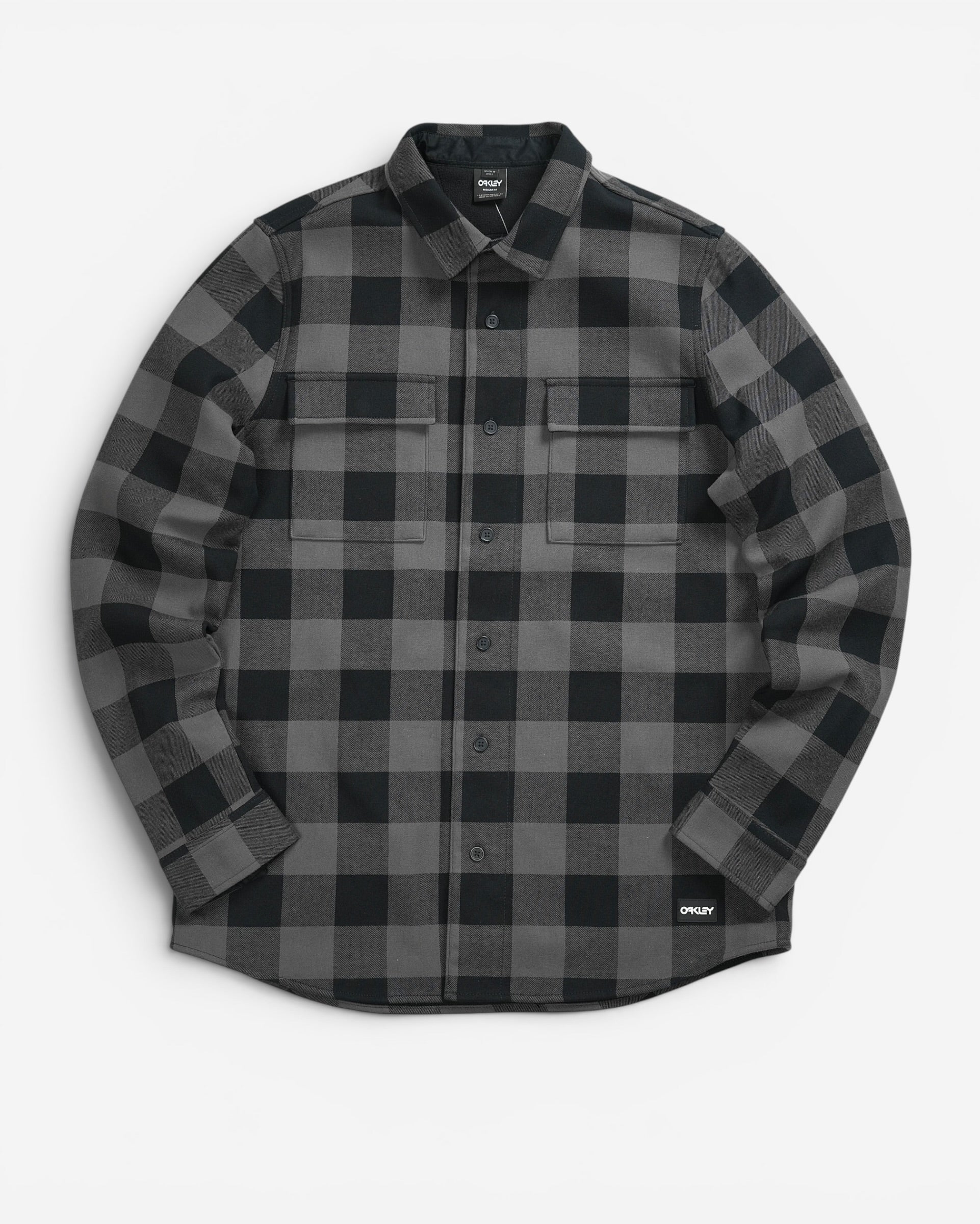 Чорно-сіра картата сорочка-жакет Oakley Bear Cozy Flannel з довгим рукавом, двома нагрудними кишенями та невеликим прямокутним патчем бренду знизу.