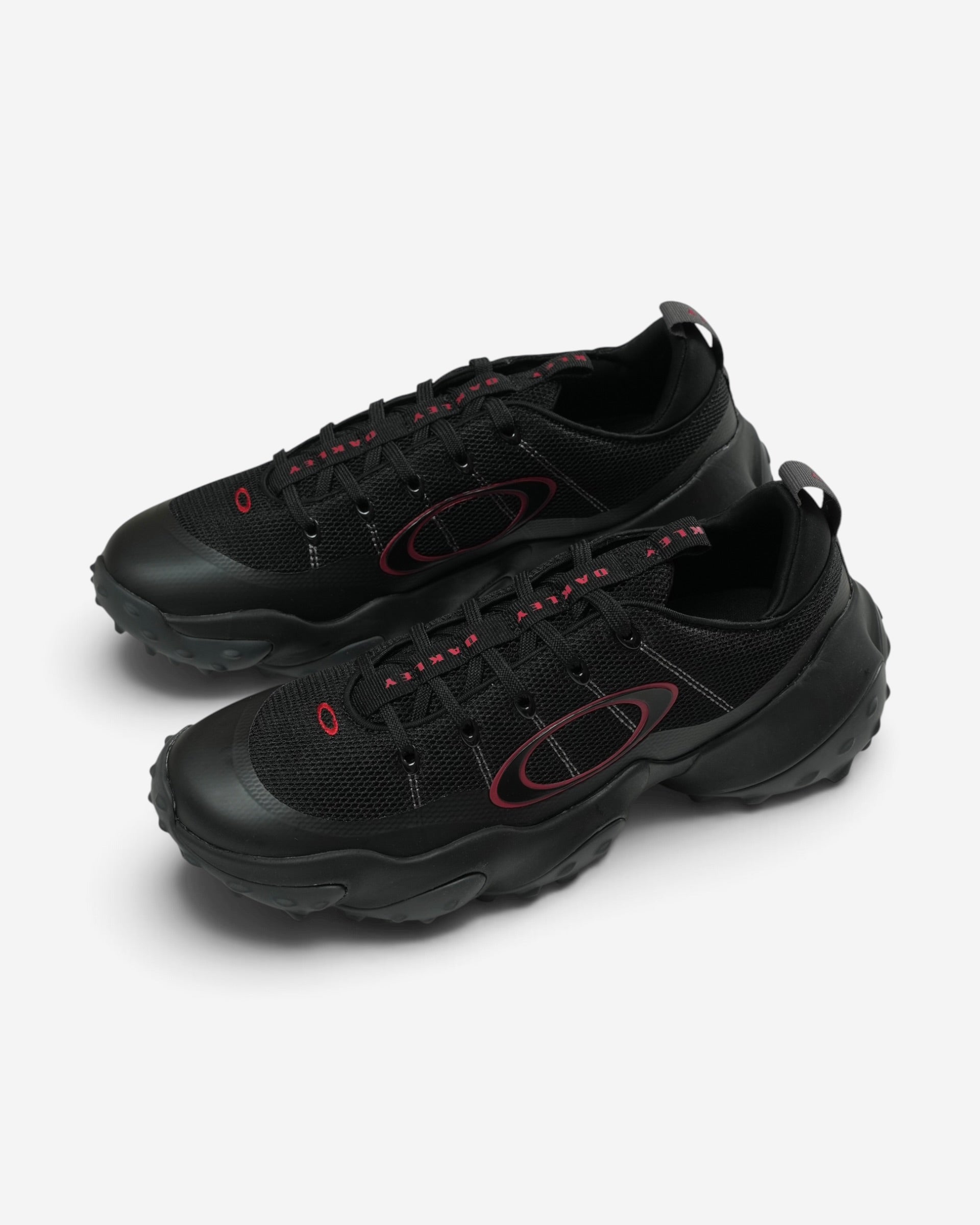 Чорні кросівки Oakley Edge Flex із масивною хвилеподібною підошвою, шнурівкою та великим бордовим контурним логотипом бренду на боці.