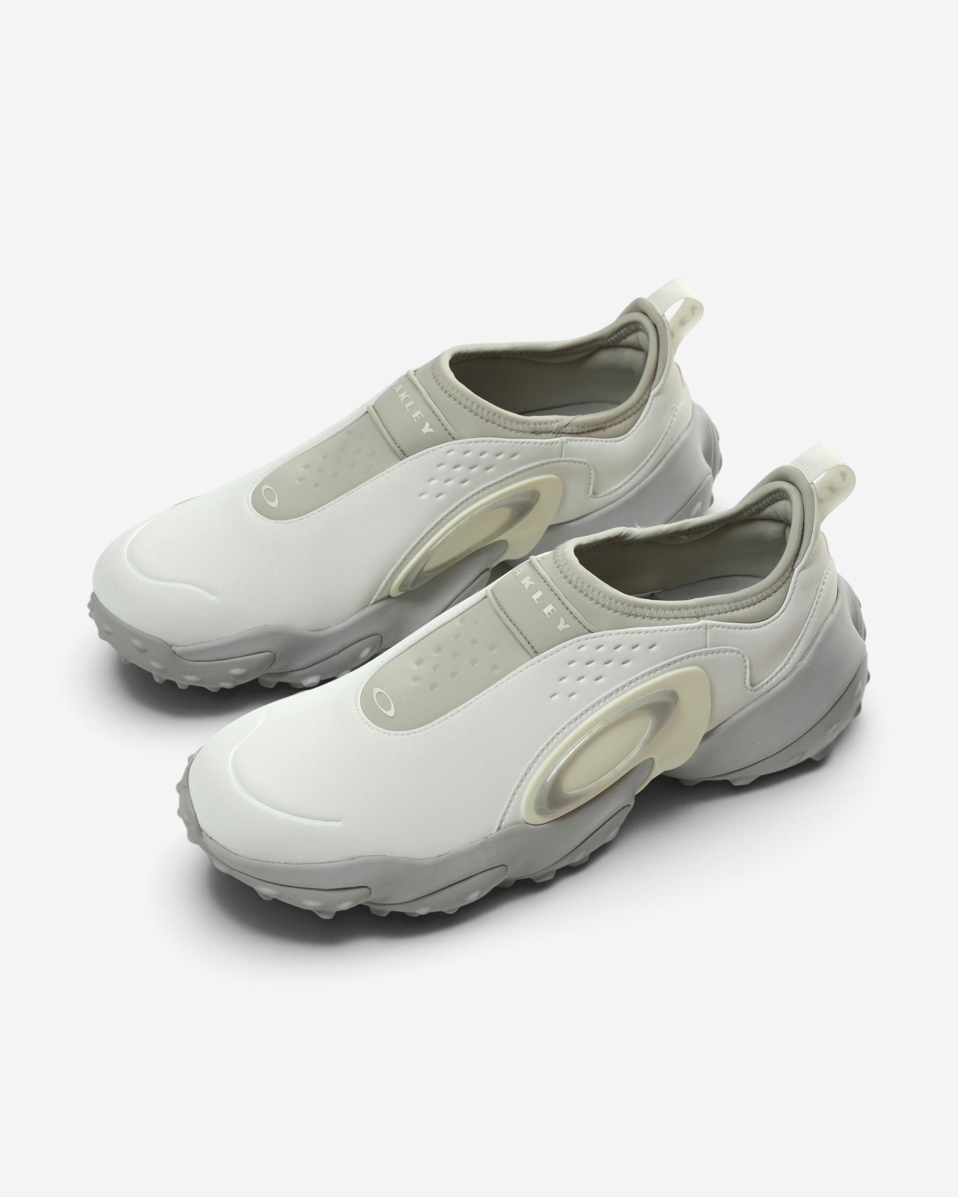 Білі чоловічі кросівки-сліпони Oakley Edge Icon з масивною сірою хвилеподібною підошвою та великим фірмовим логотипом-еліпсом на бічній панелі.