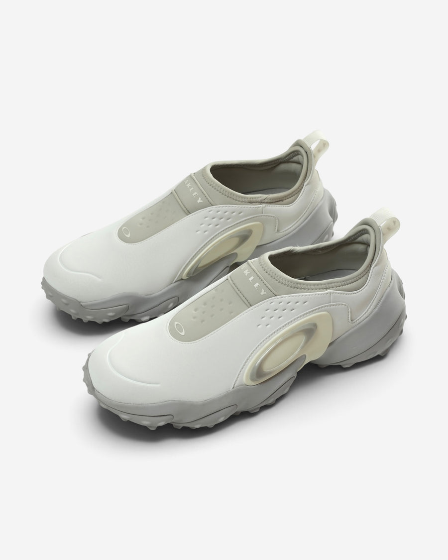 Білі чоловічі кросівки-сліпони Oakley Edge Icon з масивною сірою хвилеподібною підошвою та великим фірмовим логотипом-еліпсом на бічній панелі.